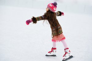 Adorable little girl in winter clothes and bobble hat skating on ice rink